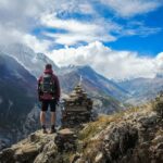 Traveling - man standing on top of mountain beside cairn stones