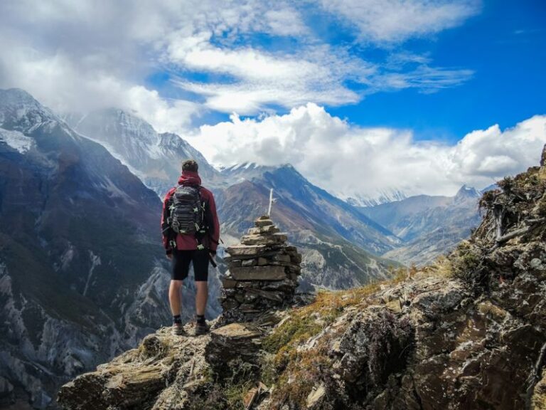 Traveling - man standing on top of mountain beside cairn stones