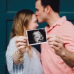New Parents - man kissing woman's forehead white holding ultrasound photo