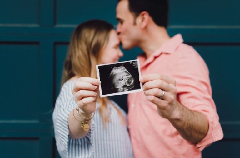 New Parents - man kissing woman's forehead white holding ultrasound photo