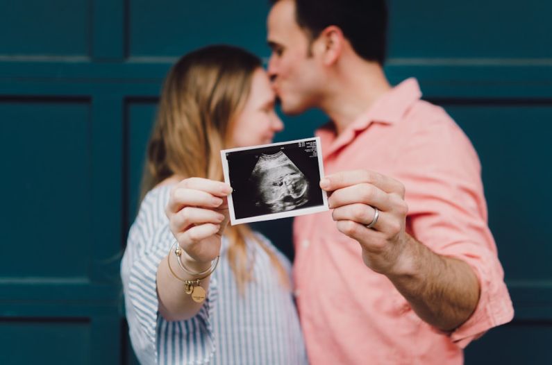New Parents - man kissing woman's forehead white holding ultrasound photo