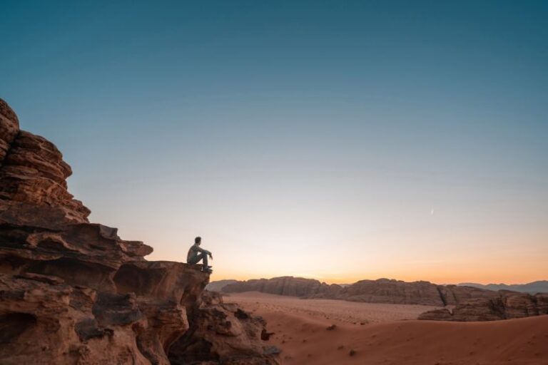 Travel - a man sitting on a rock in the desert