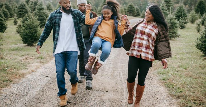 Raise Kids - Ethnic parents raising cheerful girl on tree farm roadway