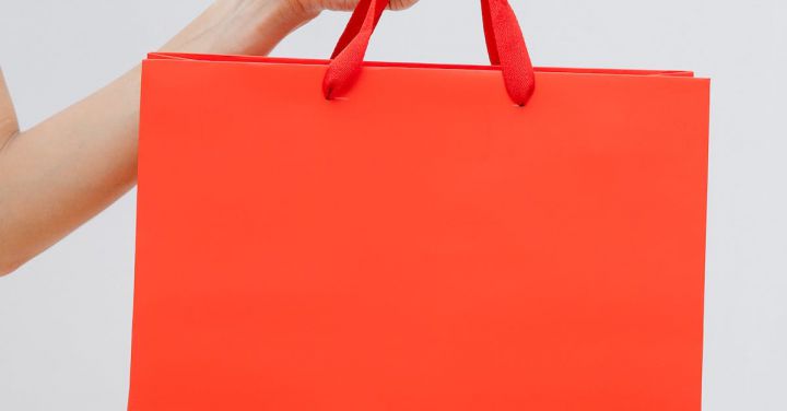 Clearance Sale - Crop unrecognizable female showing red paper shopping bag in hand against white wall