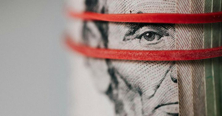 Saving Vs. Investing - Closeup of rolled United States five dollar bills tightened with red rubber band
